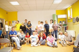 Policjanci z osobami niepełnosprawnymi pozują do wspólnego zdjęcia, w tle sala, okna