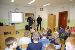 policjantka stoi z chłopcem, który trzyma misia. Miś ma na głowie plaster i bandaż na nodze