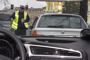 KONTROLA POJAZDU, POLICJANT ROZMAWIA Z KIEROWCĄ SIEDZĄCYM W AUCIE, W TLE ULICA I INNE POJAZDY