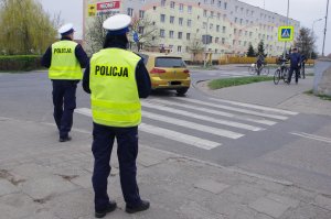 policjanci z ruchu drogowego,  w tle rowerzysta przeprowadzający rower przez przejście i pojazdy na ulicy