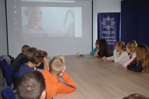 w sali konferencyjne uczniowie oglądają film w tle na ekranie kobieta po chemioterapii siedzi na łóżku szpitalnym