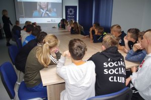 w sali konferencyjnej, uczniowie oglądają film w tle ekran i kobieta- bohaterka filmu