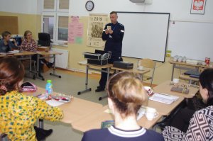 policjant prezentuje materiały edukacyjne, w tle sala lekcyjna