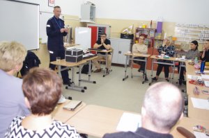policjant prezentuje materiały edukacyjne, w tle sala lekcyjna
