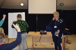 uczeń rozwiązuje kalambury, obok policjantka, w tle sala
