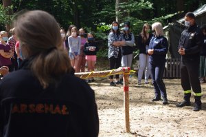 kontrolujący rozmawiają z harcerzami, w tle obóz