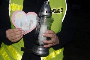 znicz i laurka w dłoniach policjantki, w tle policyjny mundur i kamizelka odblaskowa