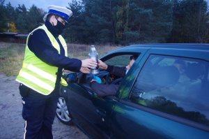 policjantka wręcza znicze, w tle droga