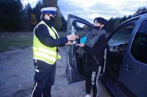 policjantka wręcza znicze, w tle droga