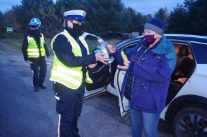policjantka wręcza znicze, w tle droga