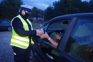 policjantka wręcza znicze, w tle droga