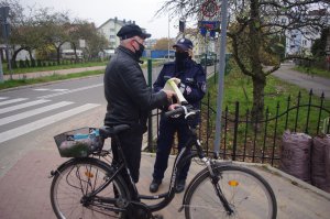 policjantka wręcza seniorowi na rowerze torbę na zakupy. W tle ulica i zabudowania
