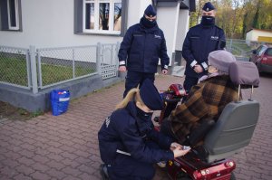 policjantka zakłada odblask na wózek inwalidzki, w tle policjanci