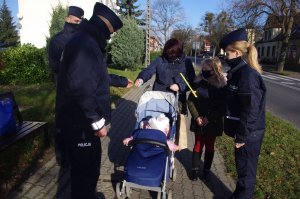 policjanci wręczają odblaski kobiecie z dziećmi, w tle ulica i zabudowania
