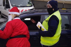 Mikołaj rozmawia z kierowcami obok policjant,  w tle zabudowania