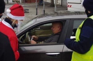 Mikołaj rozmawia z kierowcami obok policjant,  w tle zabudowania