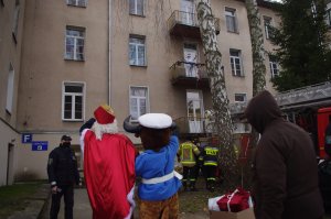 mundurowi, maskotka i Mikołaj pozdrawiają dzieci siedzące w oknach szpitla