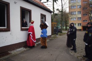 Mikołaj i maskotka podchodzą do seniorów będących w oknach