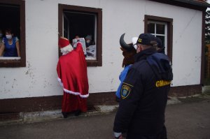 Mikołaj i policyjna maskotka rozmawiają z seniorami z okna budynku DDP i przekazują słodką paczkę