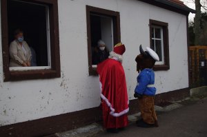 Mikołaj i policyjna maskotka rozmawiają z seniorami z okna budynku DDP i przekazują słodką paczkę