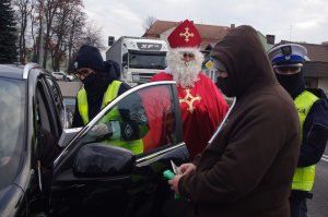 policjanci i Mikołaj rozmawiają z kierowcami i wręczają prezenty, obok zakonnik, w tle ulica