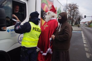 policjanci i Mikołaj rozmawiają z kierowcami i wręczają prezenty, obok zakonnik, w tle ulica