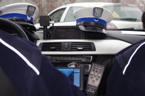 dwie czapki policyjne ułożone na desce rozdzielczej radiowozu, w tle ulica