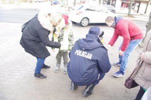 policjant wręcza odblaskowe kamizelki dzieciom, w tle rodzice