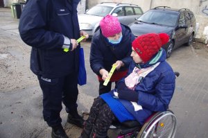 matka rozmawia z niepełnosprawną córka na wózku inwalidzkim, obok policjant, w tle zabudowania