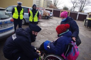 policjant zakałda odblaski na inwalidzki wózek, w tle policjanci