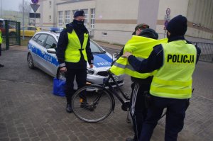 policjantka zakłada rowerzyście kamizelkę, w tle radiowóz i budynek szkoły