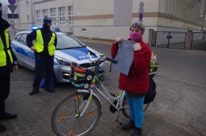 rowerzystka chwali się otrzymaną torbą,  w tle radiowóz i policjanci