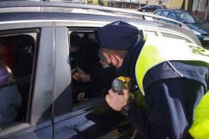 policjant wręcza dziecku maskotkę, w tle wnętrze pojazdu