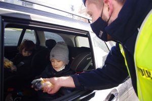 policjant wręcza dziecku maskotkę, w tle wnętrze pojazdu