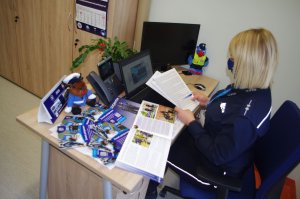 broszury, ulotki o zawodzie policjanta,  na pierwszym planie policjantka, w tle ekran laptopa, telefon