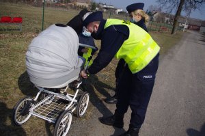 policjanci wręczają odblaski, przypinają do wózka dziecięcego  w tle zabudowania